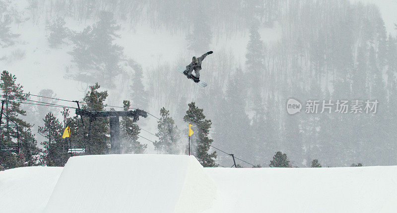 在科罗拉多州博尔德附近的埃尔多拉滑雪度假村，一个滑雪者在一个多雪的阴天里，在森林和滑雪缆车的背景下，尝试一个“正面360 Tucknee”跳跃技巧